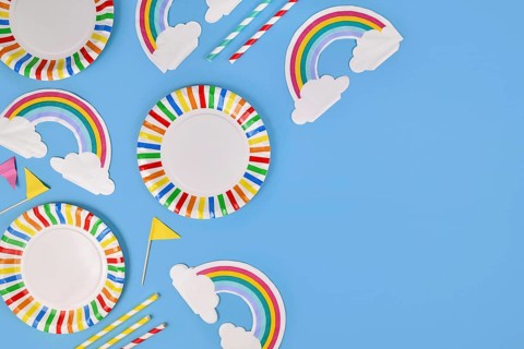 Party flat lay with colorful plates, rainbow napkins and drinking straws on blue background with