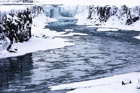 Selfoss waterfall with the river Jökullsa a Fjöllum, icy and snow-covered cliffs and shoreline,
