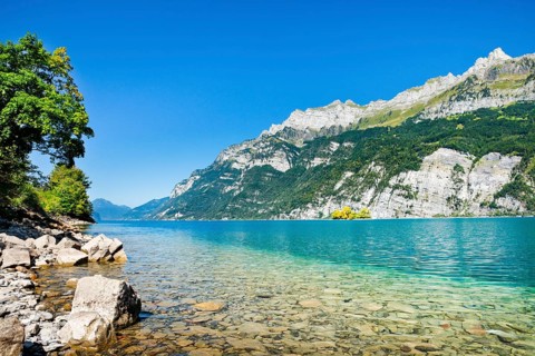 View from the shore of Lake Walen of the small chive island in the middle of the turquoise water at