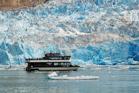 Passenger boat in front of the front of a glacier calving into the sea shimmering bluish, Tracy Arm