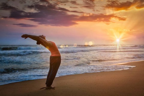 Young sporty fit woman doing yoga Sun salutation Surya Namaskar pose Hasta Uttanasana on tropical