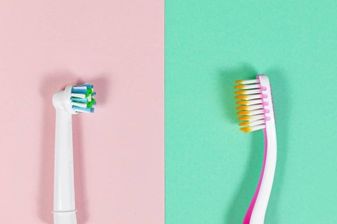 Comparison of electronic and traditional toothbrush side by side on pink and green background