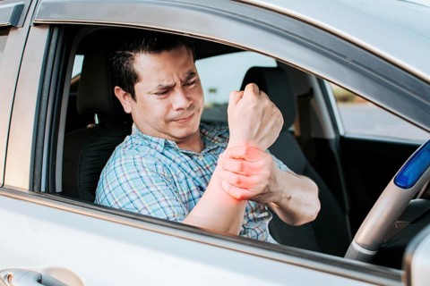 Sore driver man touching his wrist. Driver with hand pain. Suffering driver at the wheel rubbing
