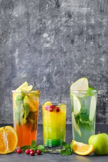 Three glasses with fruit refreshing drink on gray shabby background