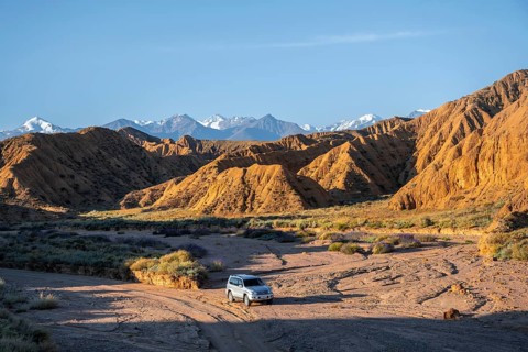 Off-road vehicle driving through a canyon, landscape of eroded hills at sunrise, badlands, white
