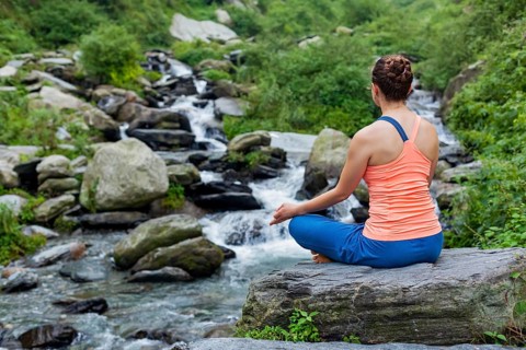 Woman in Hatha yoga asana Padmasana outdoors at tropical waterfall