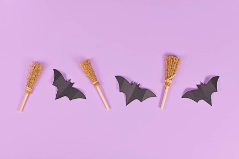 Halloween paper bats and witch brooms in a row on purple background