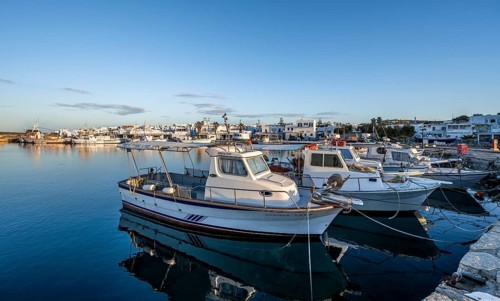 Fishing boats in the harbour of Naoussa at sunset, reflected in the sea, White Cycladic houses,
