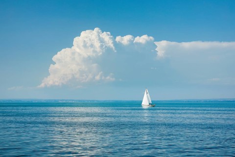 White sailboat on the turquoise water of Lake Constance with a low, large spring cloud in the