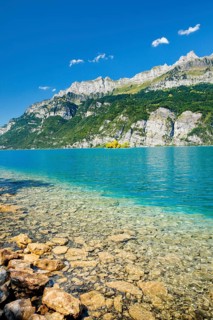 View from the shore of Lake Walen of the small chive island in the middle of the turquoise water at