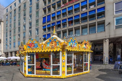 Children's carousel with painted Disney figures at the old harbour, behind skyscrapers, Genoa,