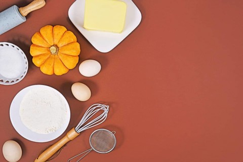 Ingredients and baking tools for pumpkin pie on brown background with copy space