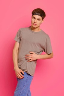 Studio portrait of young man in olive t-shirt, jeans and bandana on head over pink background