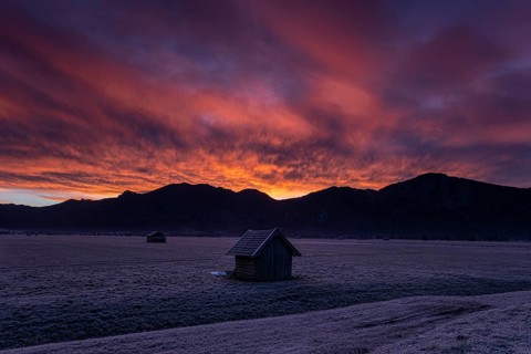 Hut in front of mountains in winter, dawn, backlight, Kochel, in the background Rabenkopf and