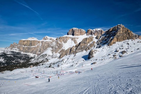 View of a ski resort piste with people skiing in Dolomites in Italy. Ski area Belvedere. Canazei,
