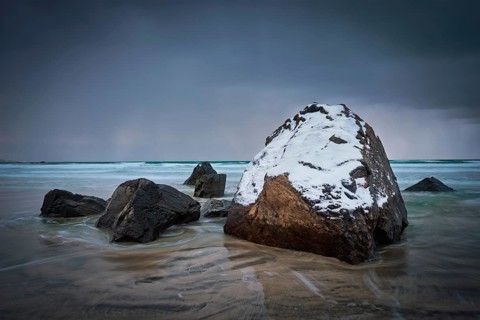 Rocks covered with snow on Norwegian sea beach in fjord in stormy weather with clouds. Skagsanden