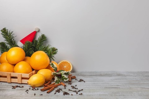 Wooden basket with oranges and lemons, cloves and cinnamon sticks, Christmassy, light background,
