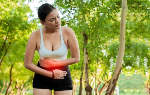 Woman in sportswear with stomach ache in a park. Running woman with digestive problems. Sport girl