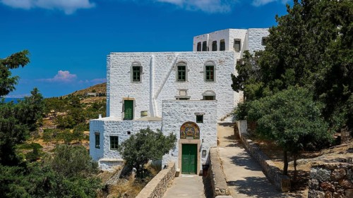 A white building with green windows and red roofs, decorated with a mosaic, in a Mediterranean