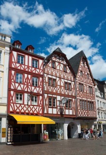 Medieval half-timbered houses in red and white with shops and passers-by under a clear sky,