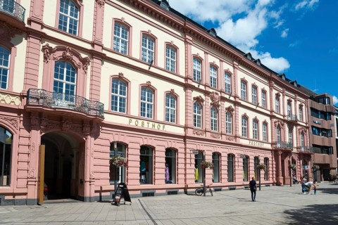 Historic building in pink and beige in the city centre with pedestrians under a blue sky, Posthof