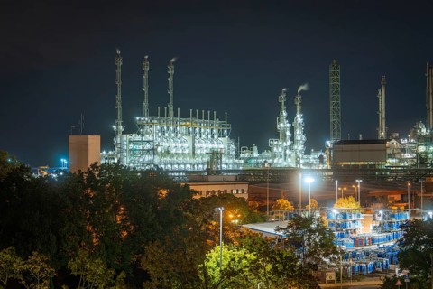 Industrial end at night with illuminated chimneys and warehouse buildings surrounded by trees and