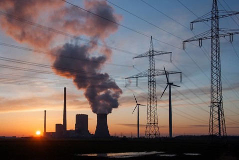 Power station, wind turbines and electricity pylons in silhouette at sunset with smoke in the sky,