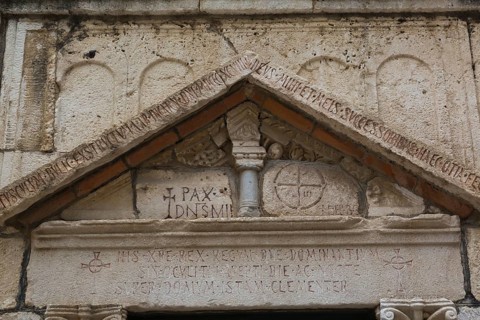 Close-up of carved letters and ancient symbols on old limestone building facade with triangular