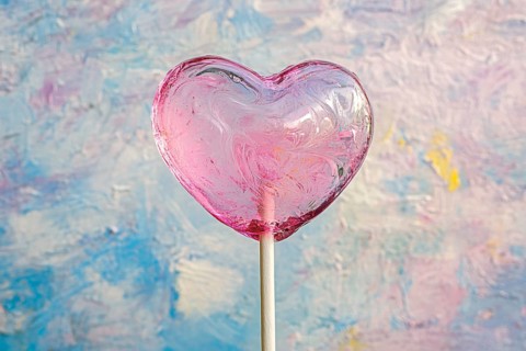 Pink heart shaped Valentine's Day lolli in front of colorful background, AI generated