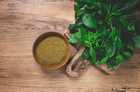 Ground green basil, in a ceramic bowl, with a bouquet of fresh green basil, on the table, top view,