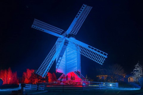 A large, blue-red illuminated windmill at night with a dark background, world of lights,
