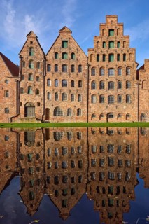 Historic salt warehouses, brick buildings reflected on the water surface of the Trave, blue sky