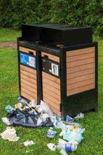 Black painted metal and natural wood garbage recycling bins with discarded thrash on green grass