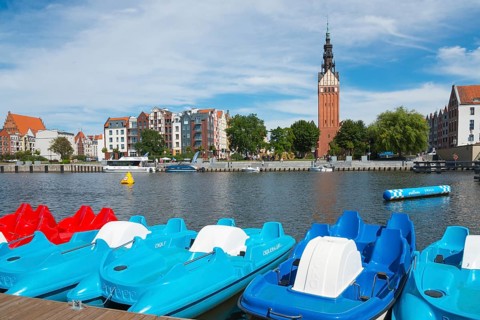 Colourful pedal boats on the river, buildings and a striking tower in the background, St. Nicholas