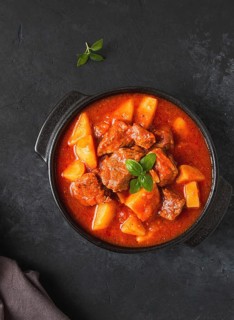 Stew with potatoes, in tomato sauce, with spices and herbs, close-up, no people, on a black