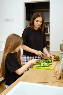 Mother and her daughter slicing organic cucumbers on wooden cutting board in the kitchen