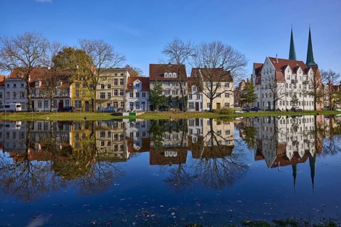 Riverbank of the Trave, historic houses, trees, church towers of Lübeck Cathedral, cloudless blue