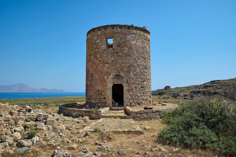 Old, abandoned mill near the coast, surrounded by rocky terrain under a blue sky, windmill, ruin,