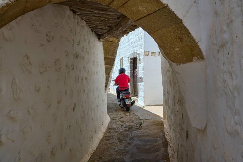 Motorcyclist riding through a narrow alley with whitewashed walls on a sunny day, Chora, main town