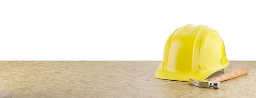 Yellow construction hard hat and hammer resting on particleboard banner isolated on a white