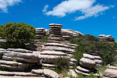 Rock formations under a clear blue sky with a few clouds and lush vegetation below, Karst