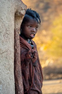 Himba girl leaning against a traditional mud hut, in the morning, traditional Himba village,