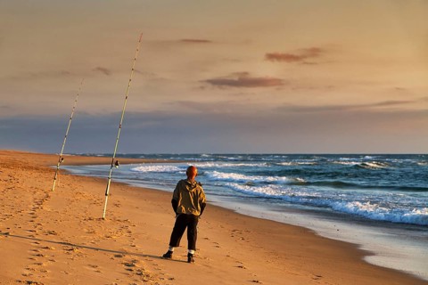 Surf fishing, angler standing with two rods on the beach, Soustons Plage, evening light, Silver