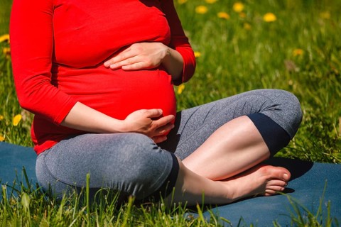 Pregnancy yoga exercise, pregnant woman doing asana Sukhasana easy yoga pose holding her abdomen