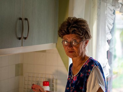 Granny with old smock apron, glasses and wig at the kitchen window in the kitchen, Germany, Europe