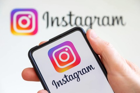 Hand holding mobile phone with Instagram logo social media with computer screen