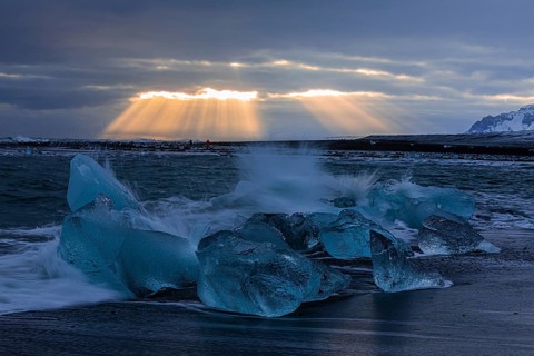 Waves breaking on icebergs on the black beach of Breidamerkursandur, sunset, near Jökullsarlon,