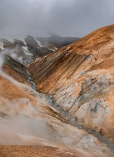 Steaming stream between colourful rhyolite mountains and snowfields, Hveradalir geothermal area,
