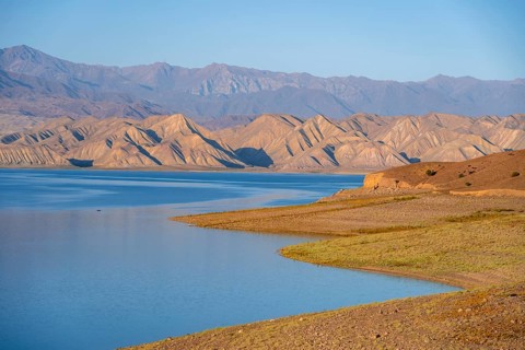 Blue Toktogul reservoir between dry mountain landscape, hilly mountains in the evening light,