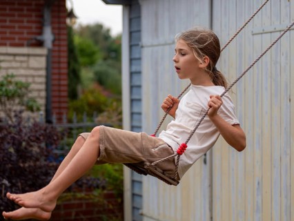 Boy swinging while sitting on children's swing at shed and garden gate, Germany, Europe